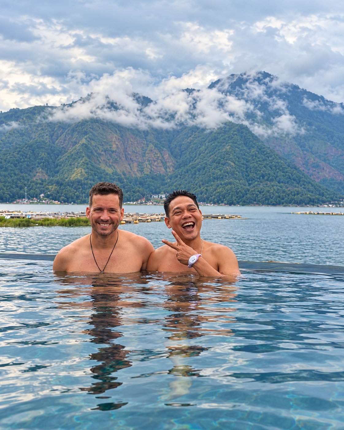 Zwei lachende Badegäste im warmen Wasser einer heißen Quelle am Batur-See, im Hintergrund der wolkenverhangene Mount Batur
